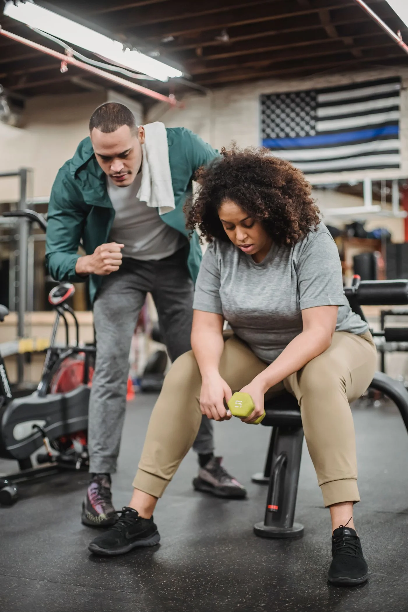 A personal trainer guiding a client through a dumbbell exercise at the gym